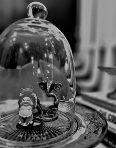 Vintage glass cloche display with decorative Buddha figurine and ornamental base in dramatic black and white photography