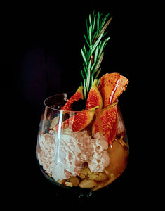 Craft cocktail garnished with fresh figs, rosemary sprig and crushed ice in wine glass against dark background