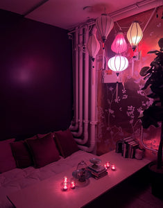 Cozy lounge room interior with white paper lanterns, burgundy velvet pillows, scattered red lighting, glass box display cases and decorative floral wallpaper